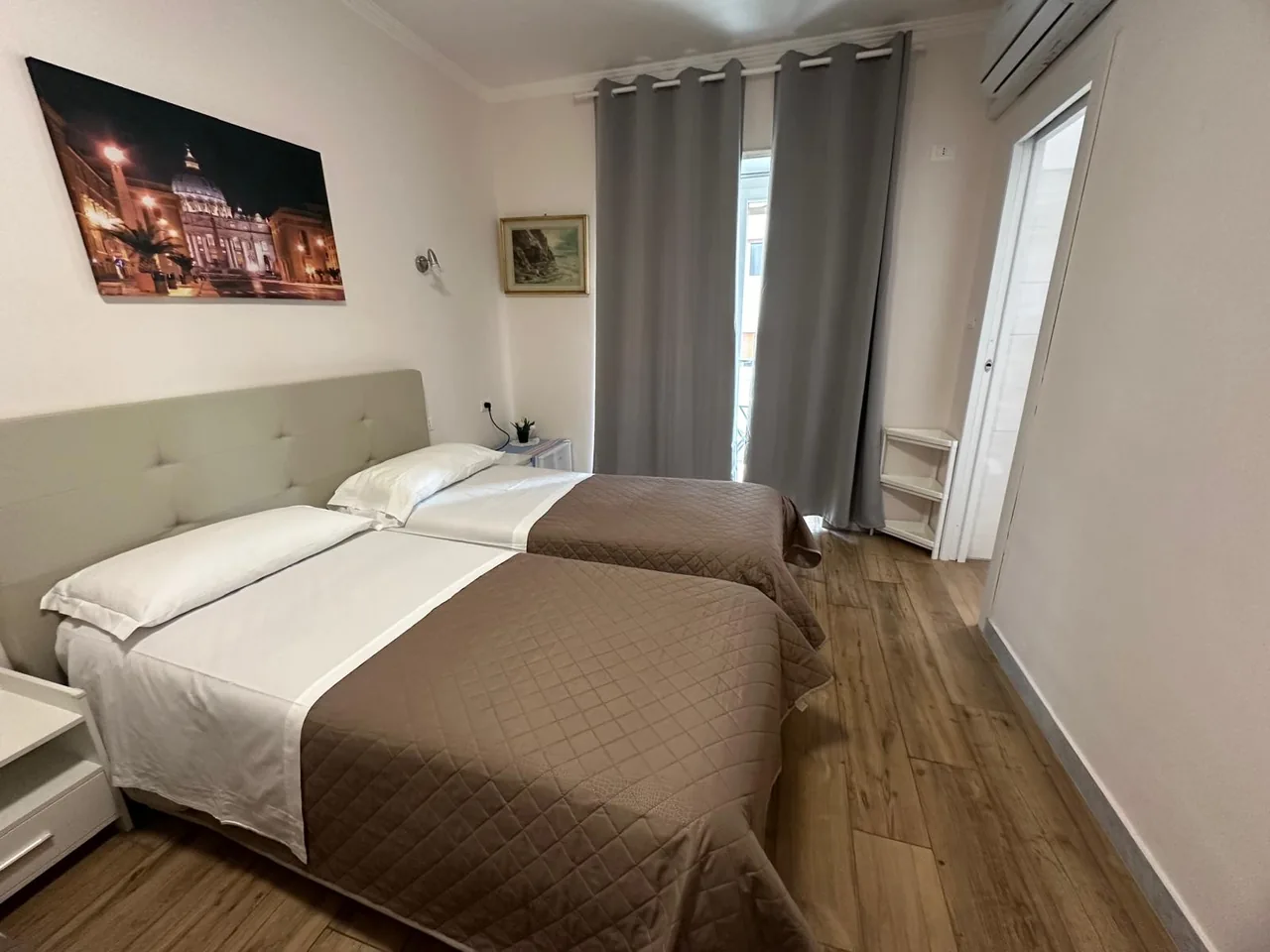 La camera con il letto matrimoniale e il letto singolo, le tende grigie e la porta-finestra