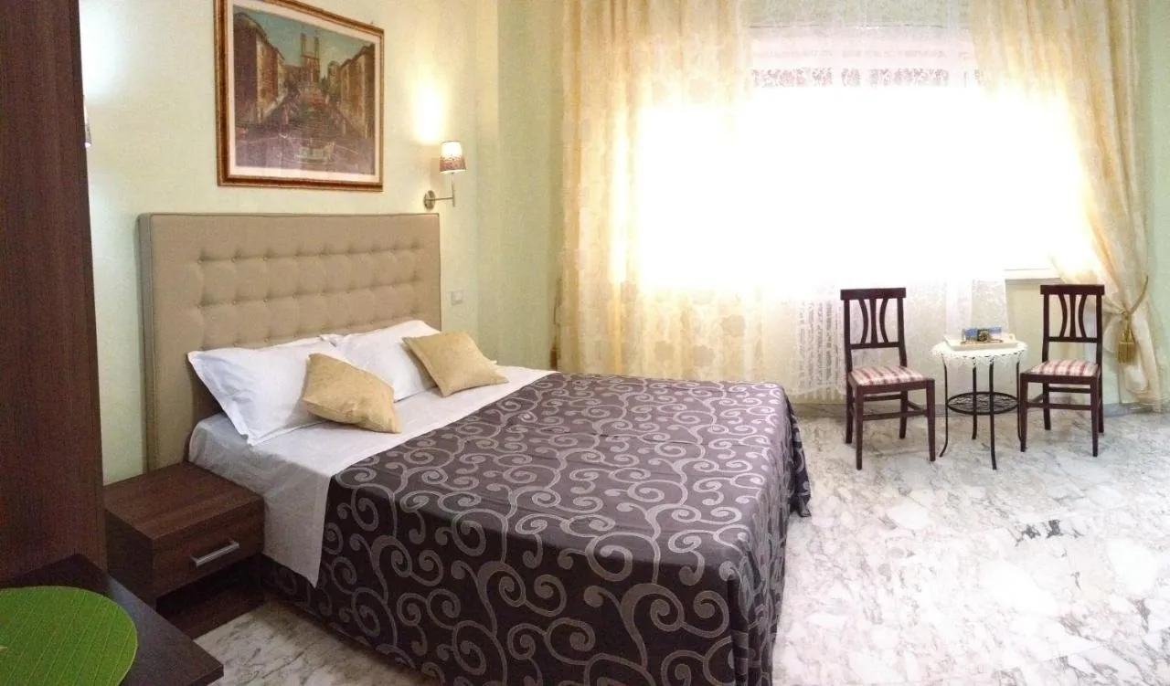 Camera con letto matrimoniale, testiera beige, pavimento chiaro e due sedie accanto alla finestra
